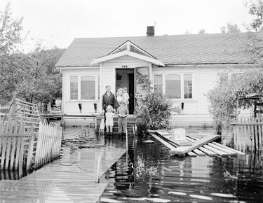 1948 Fraser River Flood - Port Mann - A family poses for a photograph in front of a house that has been surrounded by water. 1948. Vancouver Sun.