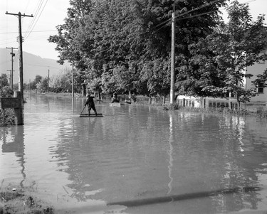 1948 Fraser River Flood - Rosedale - View of a flooded street along which a boy floats atop a make-shift raft and people paddle in a small boat. 1948. Vancouver Sun.