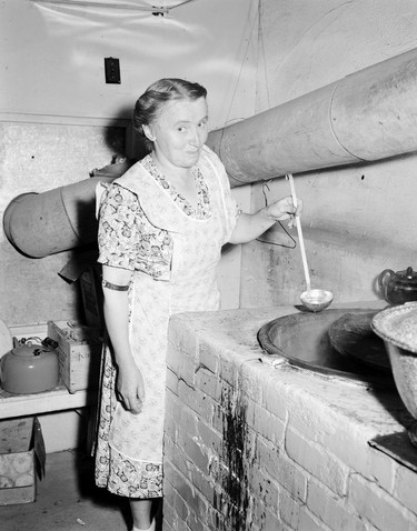 1948 Fraser River Flood - Sumas - Yarrows - A woman smiles and looks into the camera as she prepares food in a brick oven. 1948. Vancouver Sun.