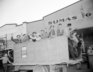 1948 Fraser River Flood - Sumas - Yarrows - A group of men wave from the back of a flatbed truck, parked outside what appears to be a Sumas auto shop. 1948. Vancouver Sun.