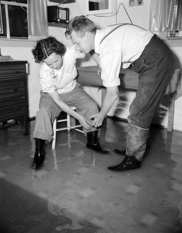 1948 Fraser River Flood - Vedder Canal - A man and woman wearing rubber boots appear to fish for something inside a flooded residence. 1948. Vancouver Sun.