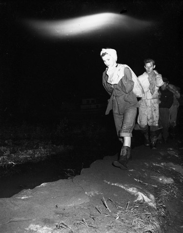1948 Fraser River Flood - Vedder Canal - A woman heads a line of people hauling sandbags at night. 1948. Vancouver Sun.