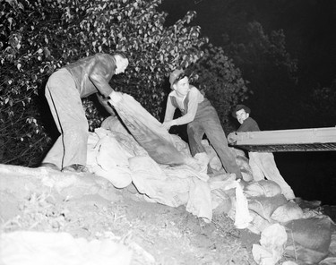 1948 Fraser River Flood - Vedder Canal - Men work outside at night unloading sandbags from a conveyor belt. 1948. Vancouver Sun.