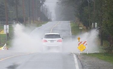 A car splashes through a huge puddle in the middle of 232 Street in Langley on Nov. 15, 2021. Many roads have been flooded, washed out or closed after two days of heavy rains have buffetted the Lower Mainland.