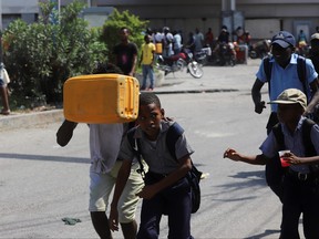 A man covers his face with a plastic container as people move away from a gas station ransacked by people angry after the station refused to distribute fuel amid a nationwide shortage, in Port-au-Prince, Haiti, Nov. 4, 2021.