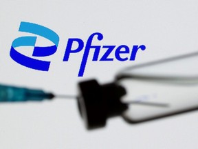 A syringe and vial are seen in front of a displayed Pfizer logo in this illustration PHOTO taken June 24, 2021.