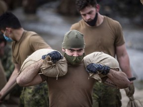 A member of the Canadian Forces carries sandbags as they build a temporary dike behind houses on Clayburn Creek ahead of a rainfall warning Environment Canada has forecast for the region which is already affected by flooding, in Abbotsford, British Columbia, on Wednesday, Nov. 24, 2021.