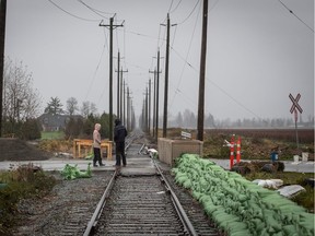 Bins of sand are placed across the road next to a wall of sandbags along rail tracks to form a temporary dike in the Huntingdon Village area of Abbotsford on Sunday, November 28, 2021.