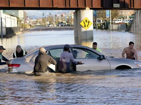 Passersby surround and push to shore a car floating in a low spot on Ferndale, Washington's, Main Street which was flooded by the Nooksack River on Tuesday, Nov. 16, 2021.