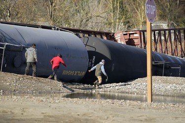 People walk by railroad cars derailed by flooding near tracks at a BNSF rail yard Wednesday, Nov. 17, 2021, in Sumas, Wash.