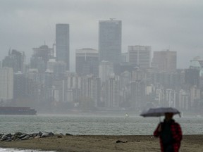 The skyline is hidden behind low cloud and rain as a pedestrian walks along Spanish Banks in Vancouver, Nov., 7, 2021.