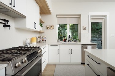 In the kitchen, oak-look laminate millwork – budget-friendly and durable – adds warmth to flat-front white cabinetry, 3-cm-thick quartz counters and a matching backsplash; complementing wide-plank laminate flooring by Mohawk, in Soft Chamois Oak.
