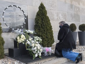 In this Dec. 6, 2020 file photo, a woman kneels in front of the commemorative plaque on the wall of Polytechnique in Montreal on the 31st anniversary of the murder of 14 women in an anti-feminist attack at Ecole Polytechnique on Dec. 6, 1989.