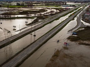 A motorist drives on a service road along the closed Trans-Canada Highway as floodwaters fill the ditches beside the highway and farmland in Abbotsford, B.C., on Wednesday, December 1, 2021.