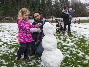Amelia Lindskoog, 4, gets help from her dad David Lindskoog building a snowman, while mom Caitlin Lindskoog looks on with Max, 6 months, on the playing fields at Aspenwood Elementary School in Port Moody.