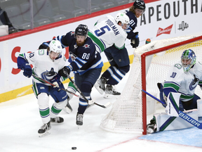 Winnipeg Jets centre Pierre-Luc Dubois (second from left) lays the lumber on Vancouver Canucks defenceman Quinn Hughes (left) in Winnipeg on Thurs., Jan. 27, 2022.