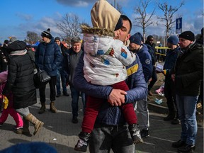 A man carries a baby as he exits a bus after arriving in Przemysl, Poland from a Polish-Ukrainian border crossing.