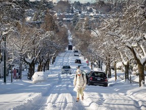 A woman bundled up for the cold weather walks up a snow-covered street after 21 centimetres of snow fell overnight, in Vancouver, on Thursday, December 30, 2021.