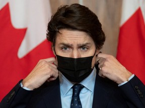 Prime Minister Justin Trudeau removes his mask as he prepares to speak during a February news conference. Even as virtually all Canadian COVID strictures are set to expire at the provincial level, Ottawa is still refusing to lift any federal mask or vaccine mandates.