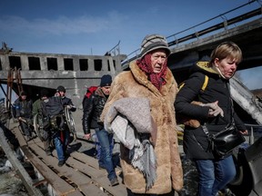 People cross the Irpin River near a destroyed bridge as they evacuate from Irpin, amid Russia’s invasion of Ukraine, outside of Kyiv, March 12, 2022.