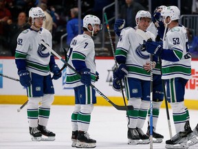 Canucks captain Bo Horvat congratulates new teammate Travis Dermott while Nic Petan (second from left) and rookie Vasily Podkolzin (far left) wait for their post-game greeting after the Canucks’ 3-1 upset victory over the NHL-leading Colorado Avalanche in Denver on Wednesday.