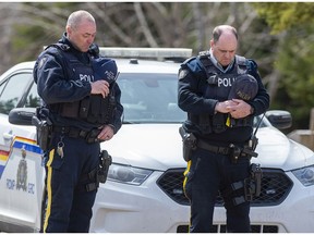 Two RCMP officers observe a moment of silence to honour slain Const. Heidi Stevenson and the other 21 victims of the mass killings at a checkpoint on Portapique Road in Portapique, N.S. on Friday, April 24, 2020.