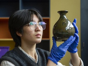 Queena Li hält eine der glasierten Flaschen mit Prägung hoch, die in versiegelten Kisten gefunden wurden, die auf dem Dachboden der Feuerhalle von Port Coquitlam verstreut waren.