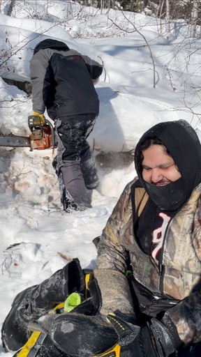 Julian Herman dries out his gear as Ron Hyggen prepares to saw wood after they got stuck for the first time on Triveet Lake in northern Saskatchewan in a February 2022 handout photo. Three cousins used traditional trapping skills and Old Spice body spray to survive a freezing night on Triveet Lake in northern Saskatchewan after their snowmobiles were stuck in slush.