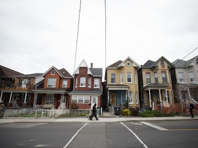 Pedestrians pass in front of houses in Toronto.