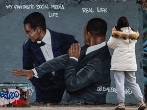 A woman takes a photo of a mural by Berlin-based street artist Eme Freethinker featuring the likeness of actor Will Smith slapping comedian Chris Rock during the Oscars ceremony, in Berlin on March 30, 2022.