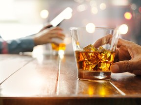 Close-up of two men clinking whiskey drink alcoholic beverage at bar counter in the pub background.