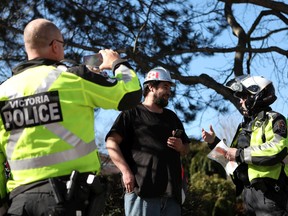 Truck driver Brian Baekgaard talks with Victoria Police after receiving a ticket for honking his horn while he joins hundreds of convoy supporters gathered at the B.C. Legislature to protest COVID-19 mandates in the province while in Victoria, B.C., on Saturday, March 5, 2022.