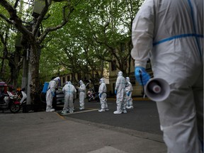 Workers in protective suits stand on a street during a lockdown, amid the coronavirus disease (COVID-19) pandemic, in Shanghai, China, April 16, 2022. REUTERS/Aly Song