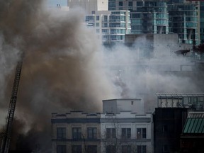 A firefighter on a ladder truck directs water on a four-alarm fire burning at a single room occupancy (SRO) hotel, in Vancouver, B.C., Monday, April 11, 2022.