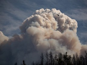 Ein Hubschrauber mit einem Wassereimer fliegt am Sonntag, dem 15. August 2021, an einer Pyrokumulus-Wolke vorbei, die auch als Feuerwolke bekannt ist und durch das Lauffeuer am Lytton Creek entsteht, das in den Bergen oberhalb von Lytton, BC, brennt.