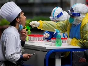 A medical worker in a protective suit collects a swab sample from a chef for nucleic acid testing, during lockdown, amid the COVID-19 pandemic, in Shanghai, China, Friday, May 13, 2022.