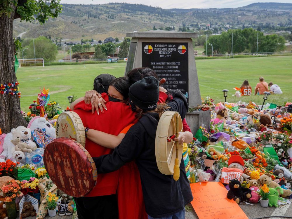 In this file photo taken on June 4, 2021 people from Mosakahiken Cree Nation hug in front of a makeshift memorial at the former Kamloops Indian Residential School to honour the 215 children whose remains have been discovered buried near the facility, in Kamloops.