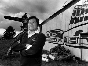 Bill Wilson on the Comox reserve with a memorial totem pole and longhouse behind him in 1983.