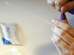 A person holds a swab while sealing a container of testing solution during a rapid antigen test for COVID-19 on Feb. 25, 2022.