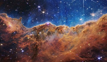 In this handout photo provided by NASA, a landscape of mountains and valleys speckled with glittering stars is actually the edge of a nearby, young, star-forming region called NGC 3324 in the Carina Nebula, on July 12, 2022 in space. Captured in infrared light by NASA's new James Webb Space Telescope, this image reveals for the first time previously invisible areas of star birth.