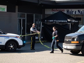 An RCMP officer moves police tape near a tent covering a body at one of three locations being investigated in regards to multiple shootings, in Langley, B.C., on Monday, July 25, 2022.