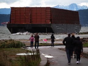 A barge that drifted loose on English Bay sits grounded on rocks during a massive windstorm, in Vancouver, on Monday, November 15, 2021. Work has finally begun in Vancouver's English Bay to remove a huge barge that has been washed up on the beach for eight months.
