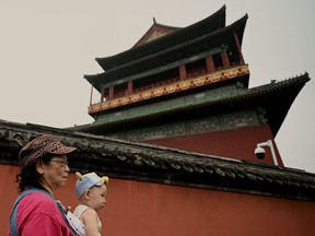 A woman carrying a baby walks in front of the bell tower in Beijing on July 27, 2022.