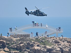 Tourists look on as a Chinese military helicopter flies past Pingtan island, one of mainland China's closest point from Taiwan, in Fujian province on August 4, 2022, ahead of massive military drills off Taiwan following US House Speaker Nancy Pelosi's visit to the self-ruled island.