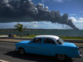 Black smoke from an oil tank on fire is seen while an old American car passes by a street in Matanzas, Cuba, on August 6, 2022.