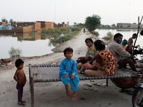 Flood victims, a family, sit along a street with the submerged houses in the background, following rains and floods during the monsoon season in Mehar, Pakistan August 29, 2022. REUTERS/Akhtar Soomro