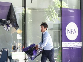 NPA signs are taken down at the civic party's Wall Centre office in Vancouver on Friday, Aug. 5, 2022. One of the men removing the signs identified himself as working for the building's strata. NPA mayoral candidate John Coupar announced he was resigning from the mayoral race early Friday.
