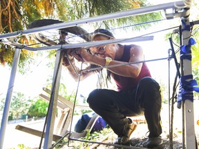Diamond Goodswimmer fixes the wheel on his cart while living in a park on Gore street in Chinatown, BC., August 10, 2022.