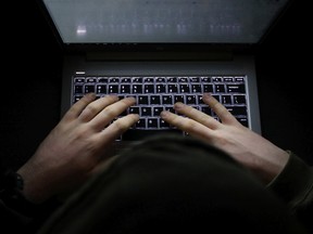 FILE PHOTO: A simple, very dark night time image of hands on an illuminated keyboard typing. Shady person wearing a hood at a computer or laptop in the dark.