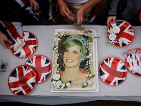 Visitors cut a cake depicting late Britain's Princess Diana in front of Kensington Palace, in central London, on August 31, 2022 during a gathering to pay a memorial tribute on the 25th anniversary of the Princess of Wales's death. CARLOS JASSO / AFP